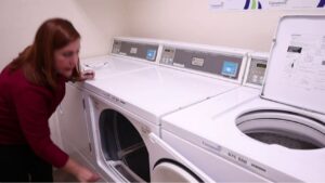 Homeowner performing simple washing machine maintenance: redistributing clothes, leveling the washer, cleaning the drain pump, and tightening loose panels in a clean laundry room.
